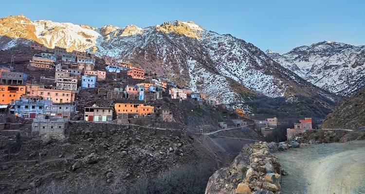 Ein Bergdorf am Hang mit bunten Häusern und schneebedeckten Gipfeln im Hintergrund.
