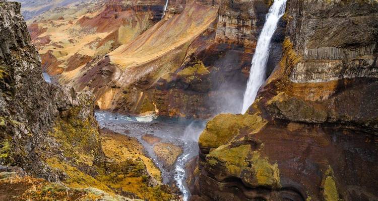 Hoge waterval die over een rotsachtige klif in een smalle canyon in het kleurrijke Ijslandse Hoogland stort.
