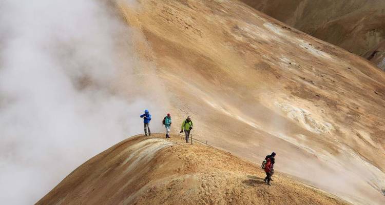 Wandelgroep die langs een dampende geothermische bergrug loopt, gedeeltelijk verscholen door opstijgende mist.