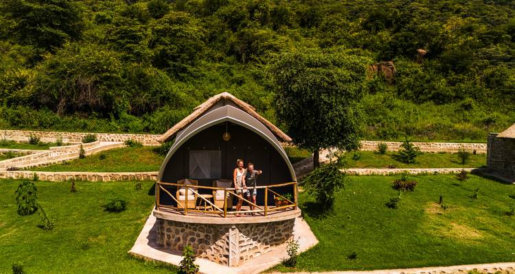 Tourists on the balcony of a thatched-roof cottage surrounded by greenery.