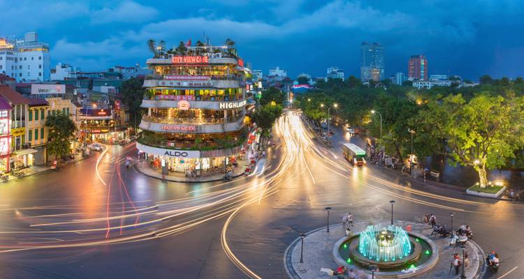 Bustling street intersection in Hanoi with neon lights at dusk.