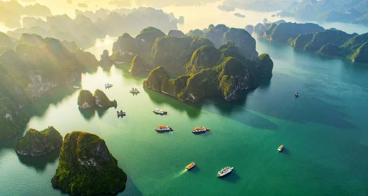 Aerial view of karst formations and boats in Halong Bay at sunset.