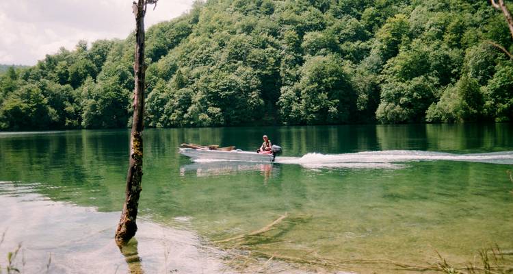 Personne dans un bateau sur un lac serein entouré d'une forêt luxuriante.