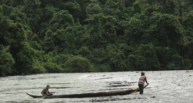 Deux personnes dans un bateau étroit sur une rivière tropicale avec une végétation dense.