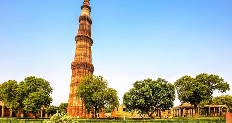 Der Qutub Minar Turm ragt über Gärten unter klarem blauen Himmel auf