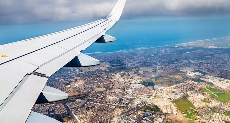Blick aus einem Flugzeugfenster über eine Küstenstadt.