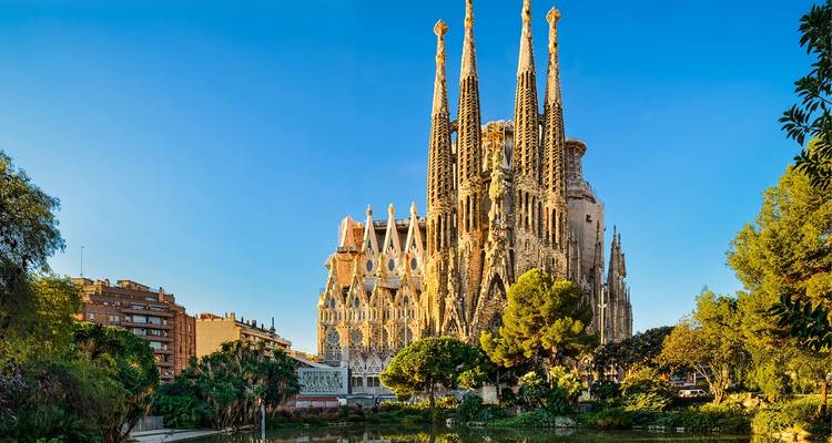 Iconische Sagrada Família basilica torens rijzen uit boven groene parkbomen onder kristalhelder Barcelona lucht.