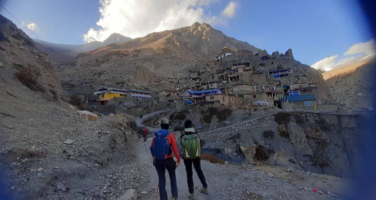 Hikers walking towards a mountain village nestled in a rocky landscape.