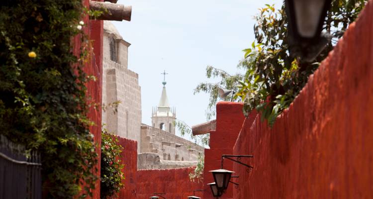 Blick auf einen Kirchturm über roten Innenhofmauern.