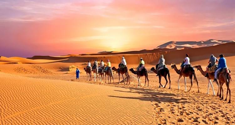 Eine Kamelkarawane, die bei Sonnenuntergang durch Sanddünen wandert.