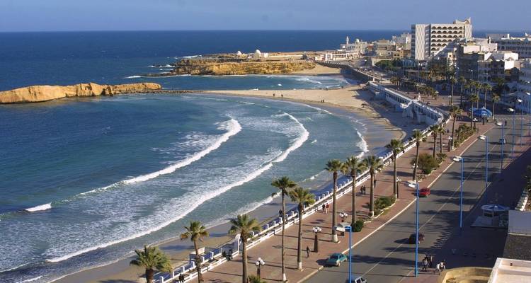 A coastal city with a promenade, sandy beach, and blue sea.