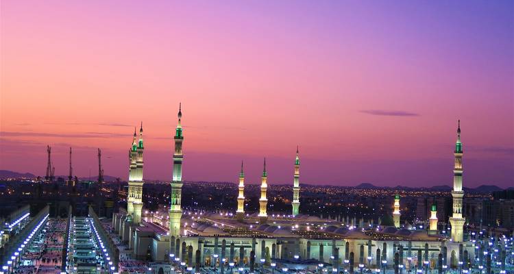 A beautifully lit mosque at sunset with a sprawling urban landscape in the background.