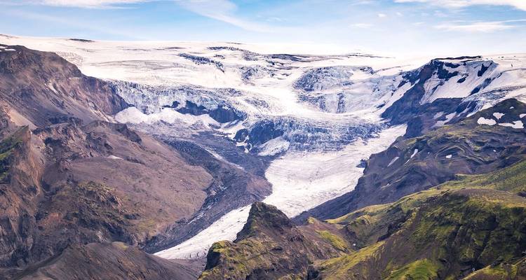 Expansive view of rugged mountains and a massive icecap with crevasses under clear blue sky.