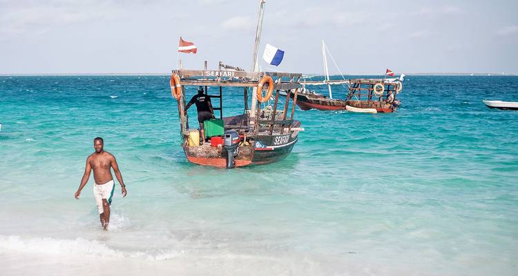 Homme entrant dans l'eau en provenance de l'océan Indien turquoise en direction de bateaux dhow en bois au large de la plage de Zanzibar