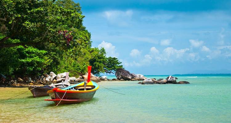 Bote de cola larga colorido anclado en agua turquesa poco profunda contra la orilla frondosa e islas distantes.