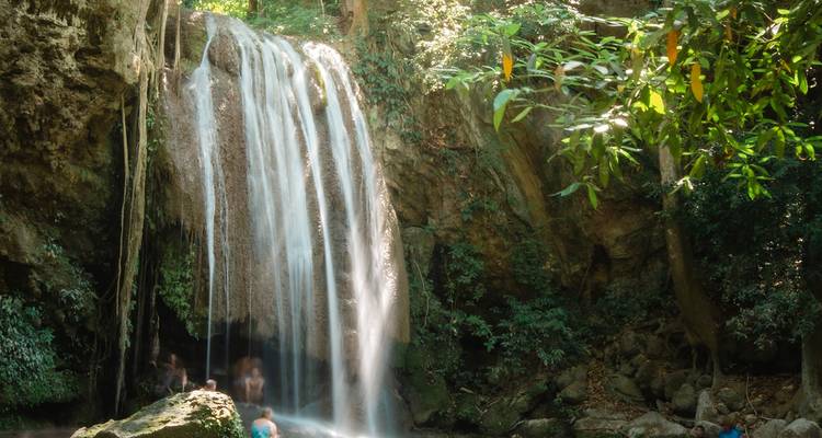 Wasserfall in einem üppigen Wald mit schwimmenden Menschen.