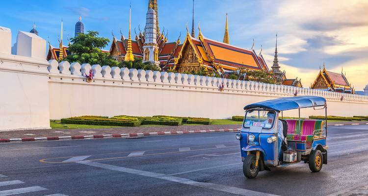 Tuk-tuk die voorbijrijdt langs een tempelmuur in een stadsstraat.