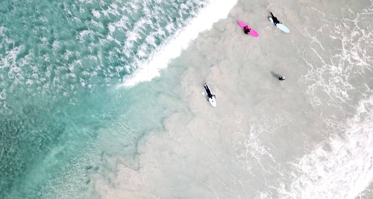 Vista aérea de surfistas en una playa con olas rompiendo cerca.