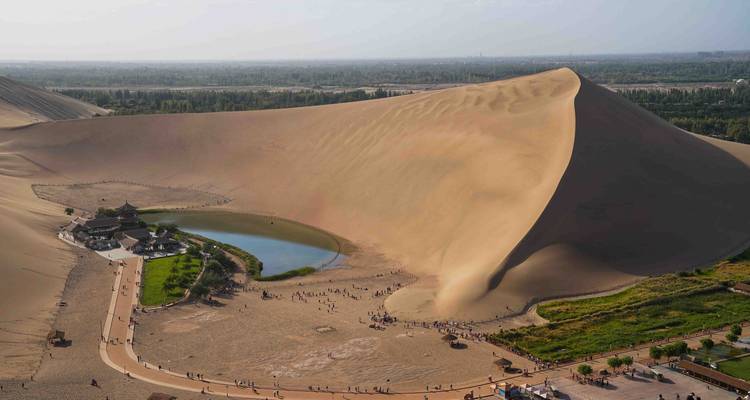 Grote zandduin met een klein meer en mensen aan de voet ervan.