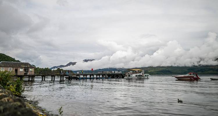 Bewölkter Tag an einem See mit einer angedockten Fähre und einem Steg.
