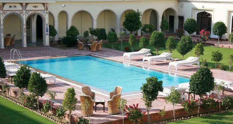 Hotelzwembad omringd door tuin met ligstoelen.