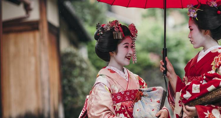 Zwei Frauen in traditioneller Kleidung mit einem roten Regenschirm.