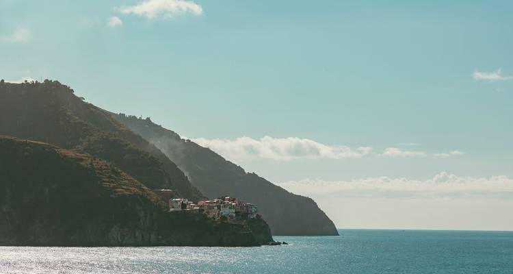 Coastal view of a Cinque Terre village perched on a cliff with sparkling turquoise sea and rugged hills.
