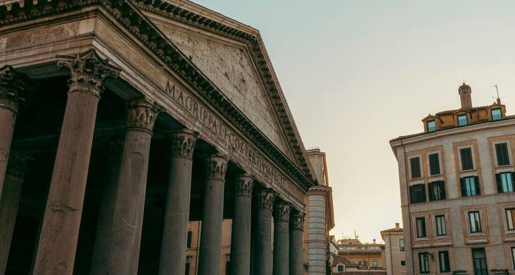 Grand facade and columns of the Pantheon in late afternoon light with adjacent Roman buildings.