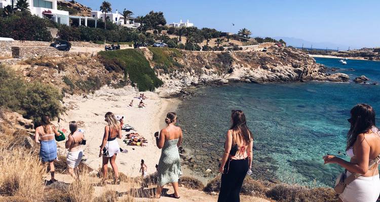 People walking towards a beach with clear waters and rocky coastline.