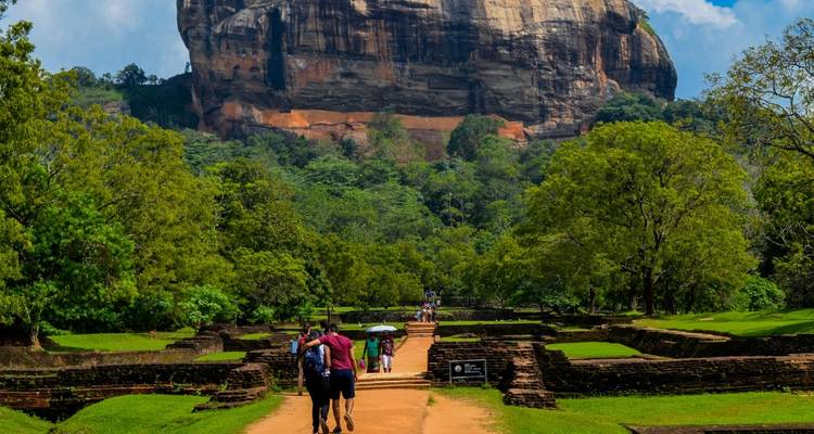 Visitors walking toward the towering Sigiriya rock fortress through lush gardens