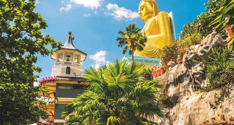 Golden seated Buddha statue towering above palm trees at a hillside temple