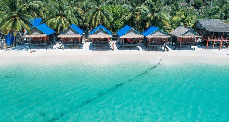 Huts with blue roofs on a beach with clear turquoise water.