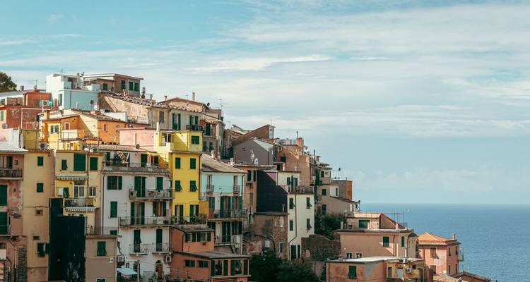 Colorful cliffside houses of Cinque Terre cascade toward the blue Ligurian Sea under a bright sky.