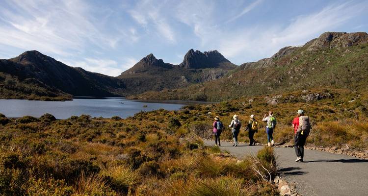 Un petit groupe de randonneurs suit un sentier pavé le long d'un lac tranquille encadré par les pics de la Cradle Mountain.