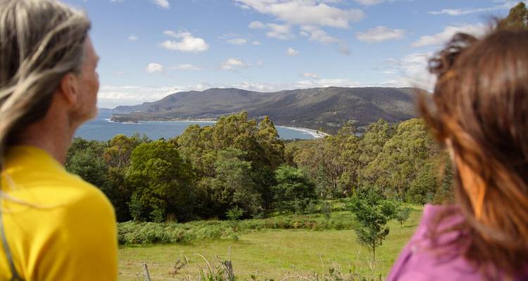Twee reizigers genieten van uitgestrekte kustbossen en baaien vanaf een uitkijkpunt op een heuveltop in Tasmanië.
