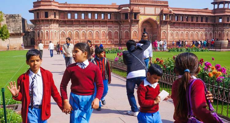 School kids in uniform walking in a garden with a historical building.