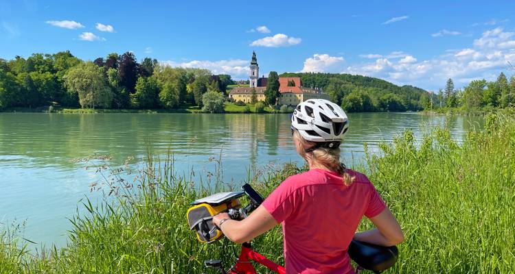 Radfahrer blickt über den Fluss zu einem entfernten Gebäude.