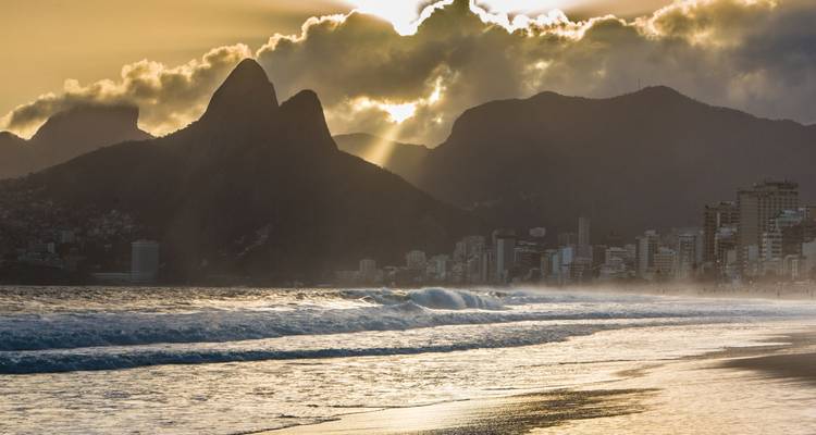 Coucher de soleil doré sur la plage d'Ipanema avec les silhouettes des pics de Dois Irmãos et de la ligne d'horizon de Rio.