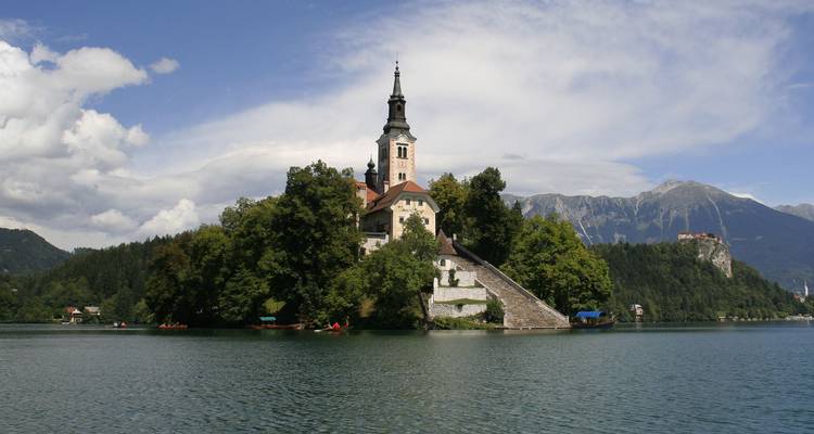 Island church on Lake Bled surrounded by alpine mountains and reflective waters.