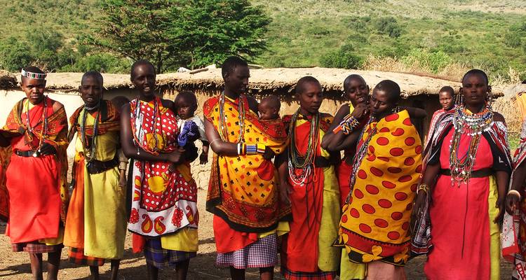 Groep Masai vrouwen en baby's in felgekleurde shukas buiten traditionele hutten.