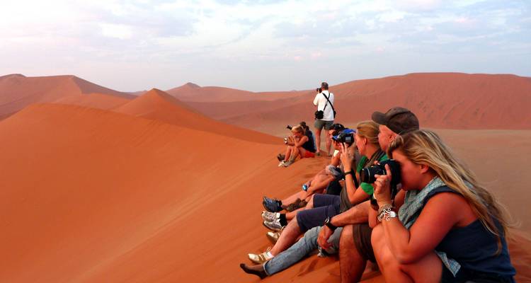Groupe de personnes assises sur une dune de sable en train de prendre des photographies.