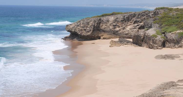 Een zanderig strand met rotsachtige kliffen en oceaangolven.
