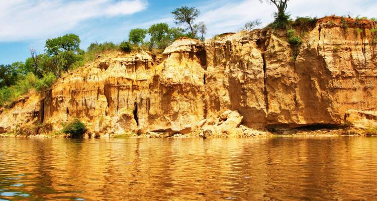 Acantilados de ocre escarpados reflejados en aguas tranquilas del río bajo un cielo parcialmente nublado.