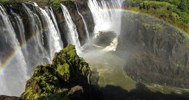 Les chutes Victoria avec un arc-en-ciel et de la brume s'élevant de l'eau.