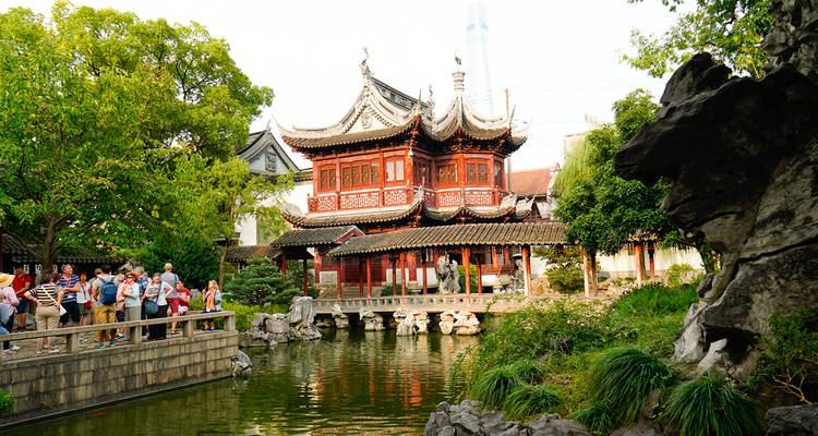 Traditional Chinese garden with a pond and tourists.