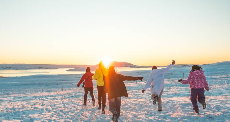 Groep vrienden rent vrolijk door besneeuwd landschap richting lage zon.