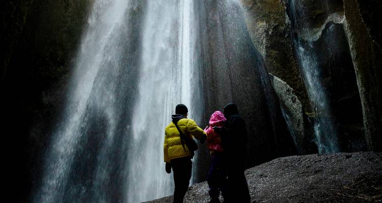 Familie bewondert torenhoge waterval vanuit grot-achtige nis achter de waterval.