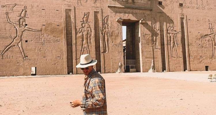 Mann, der vor einem großen antiken Tempel mit geschnitzten Figuren steht.