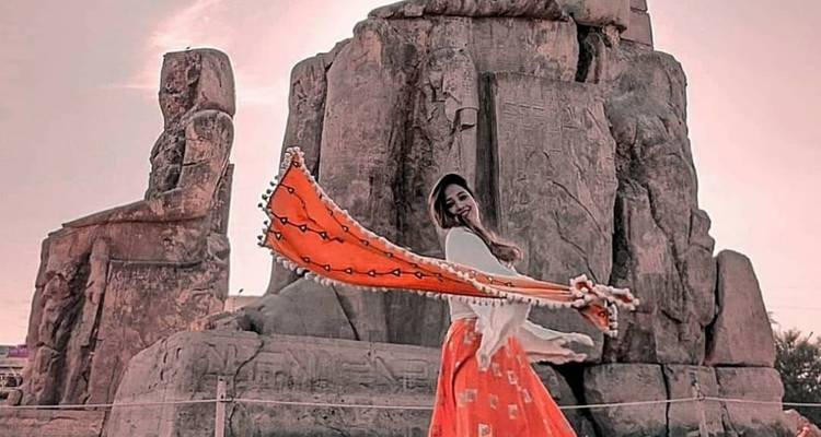 Frau in einem fließenden Kleid posiert vor antiken Steinstatuen.