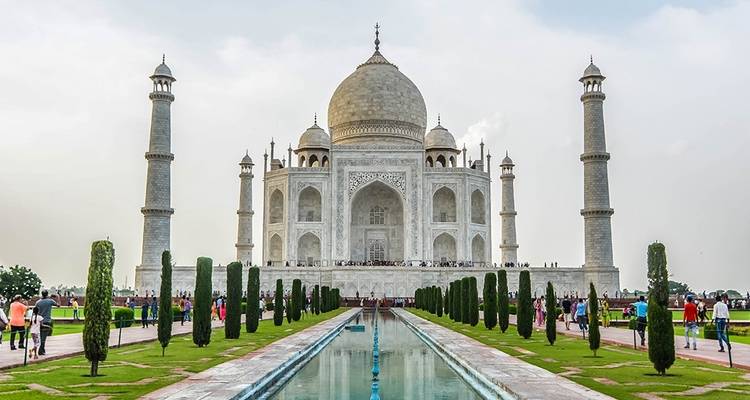 Taj Mahal mit einem Spiegelbecken davor und Besuchern, die es erkunden.
